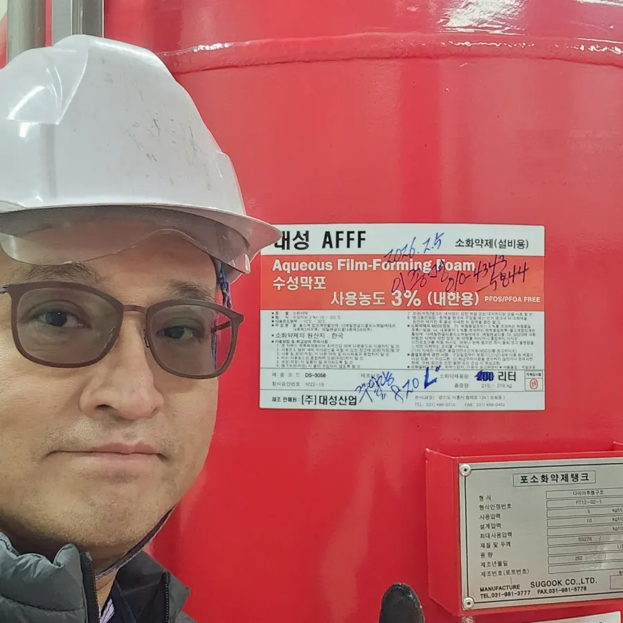 수성막포 라벨과 탱크 명판이 보이는 폼탱크 앞에서 안전모를 쓰고 확인하는 담당자